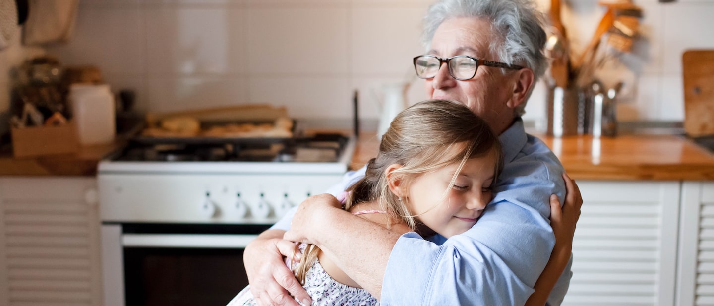 Foto: Oma sitzt in Küche und hält Enkeltochter im Arm