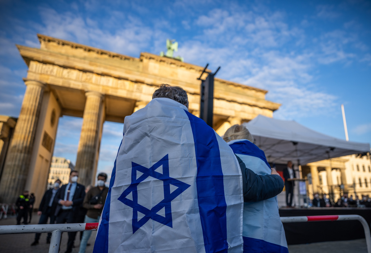 Foto: Teilnehmer an einer Demonstration zur Solidarität mit Israel stehen eingehüllt in die Flagge Israels vor dem Brandenburger Tor.